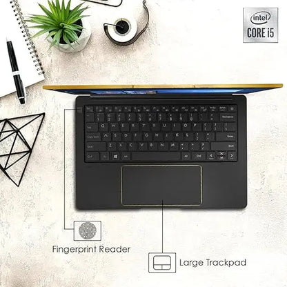 Black Avita Liber V laptop with full keyboard, large trackpad, fingerprint reader, and thin gold-colored accents on desk.